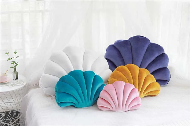 A collection of velvet shell print throw pillows in shades of purple, white, yellow, and teal resting on a white surface.