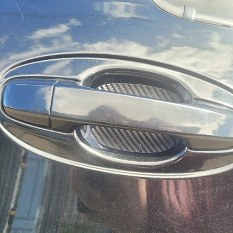Close-up of a silver car door handle with black carbon fiber protective covers installed.