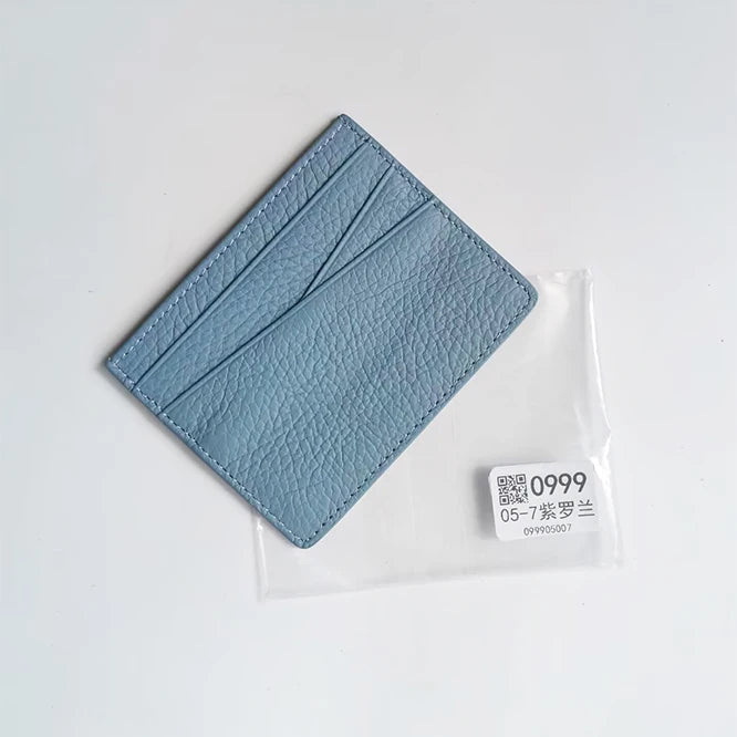 A light blue genuine leather slim card holder wallet folded and placed in a clear plastic sleeve.