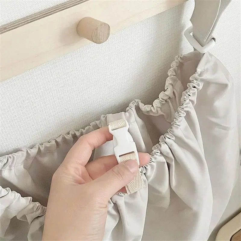 A hand is holding a white bear-themed stroller organizer with a light beige strap against a light gray fabric background.