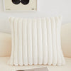 A white, vertically ribbed plush decorative pillow cover resting on a light-colored sofa.