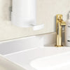 A modern gold soap dispenser and a white wall-mounted soap bar grinder above a white bathroom sink.