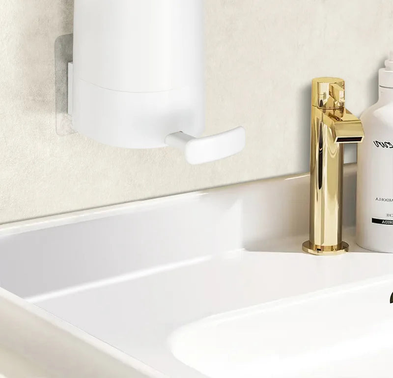 A modern gold soap dispenser and a white wall-mounted soap bar grinder above a white bathroom sink.