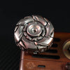 A close-up of a metallic fidget spinner with intricate, faceted design resting on a wooden surface.