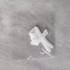 A white fabric bow tied in a knot resting on a clear plastic sheet against a gray marbled surface.