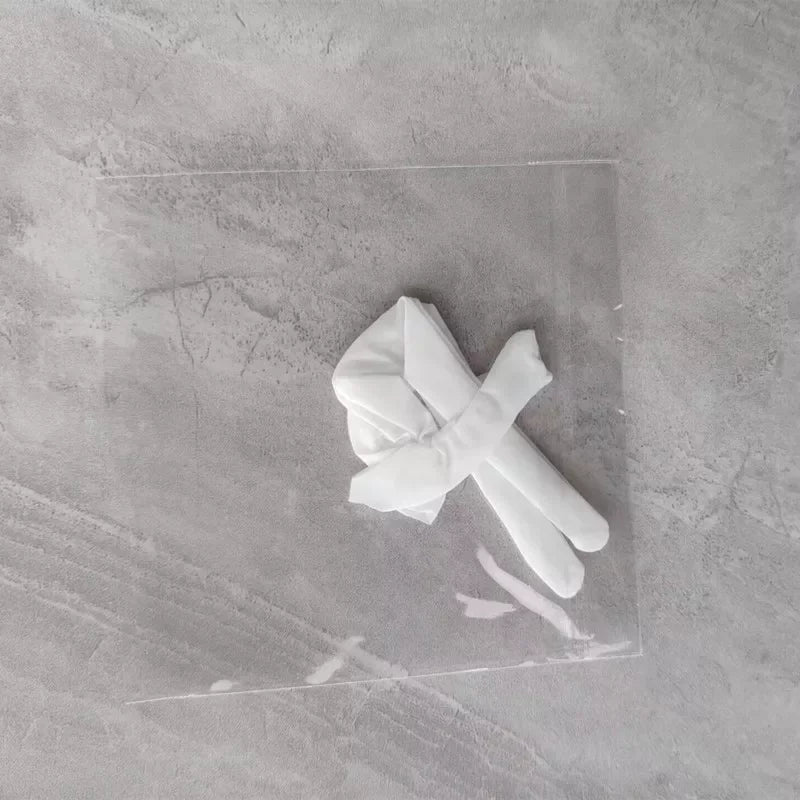 A white fabric bow tied in a knot resting on a clear plastic sheet against a gray marbled surface.