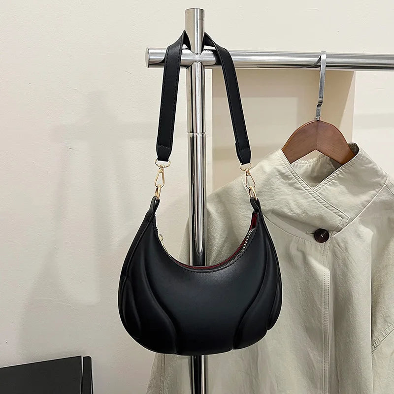 A black textured crossbody bag with a gold-tone adjustable strap is displayed on a hanger against a light background.