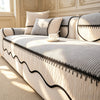A cream striped chenille sofa cover with a pleated black hem and decorative piping on a light-colored upholstered bed.