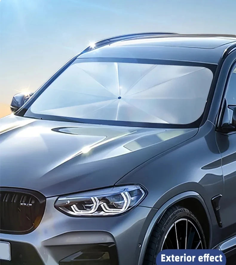 A silver SUV's front windshield is covered with a clear, foldable sunshade for UV protection.