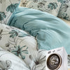A teal and grey watercolor floral duvet cover set displayed on a bed with a white washing machine nearby.