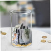 A clear glass cylinder filled with various coins and banknotes sitting on a white surface.