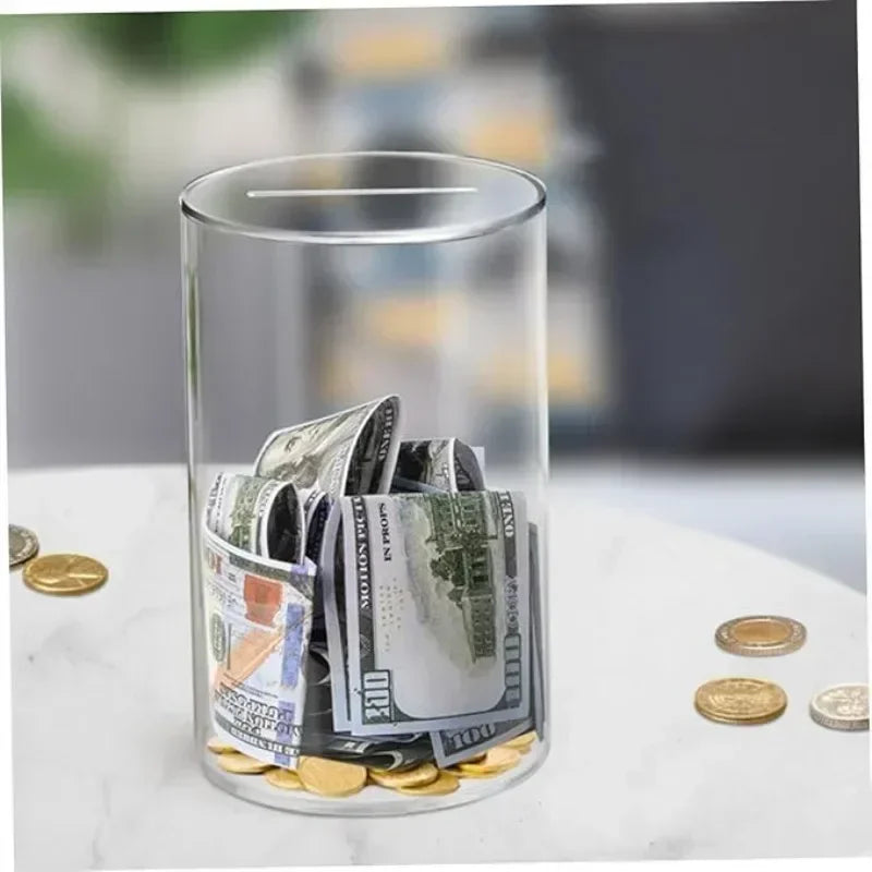 A clear glass cylinder filled with various coins and banknotes sitting on a white surface.