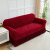 A deep red jacquard sofa cover with an elastic skirt displayed on a white modern sofa.