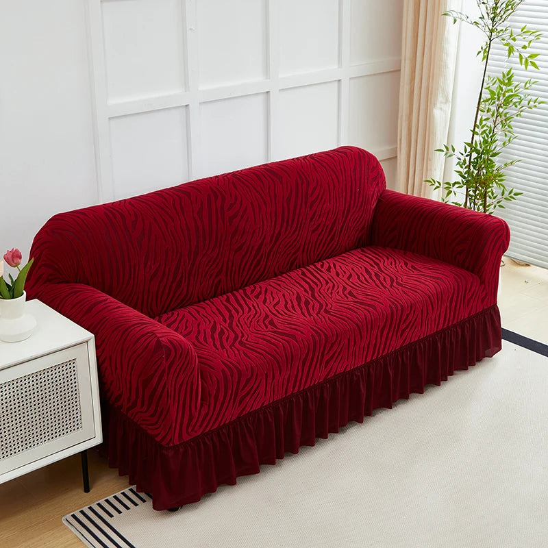 A deep red jacquard sofa cover with an elastic skirt displayed on a white modern sofa.