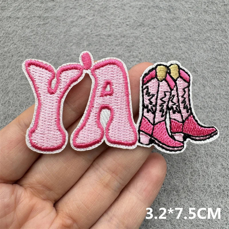 Pink embroidered iron-on patches shaped like the letters Y and A along with a pair of pink boots