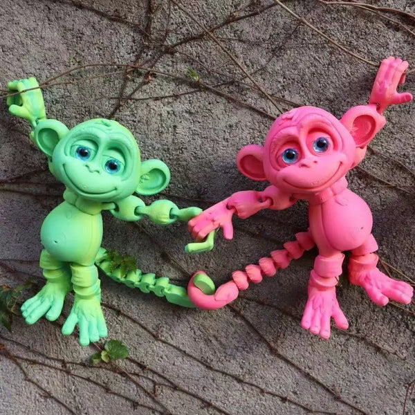 A pair of playful 3D printed monkey statues, one green and one pink, are positioned against a textured background.