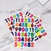A collection of colorful rainbow dot stickers featuring numbers and letters scattered on a white marble surface.