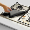 A hand is placing a black square liner protector onto a gas hob grate.