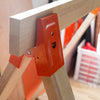 Close-up of an orange steel bracket attached to a light wood workbench frame.