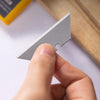 A hand holds a silver T-shaped utility knife blade against a white background.