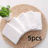 Five white soft cotton terry cloth face towels arranged on a woven mat next to a small green plant.