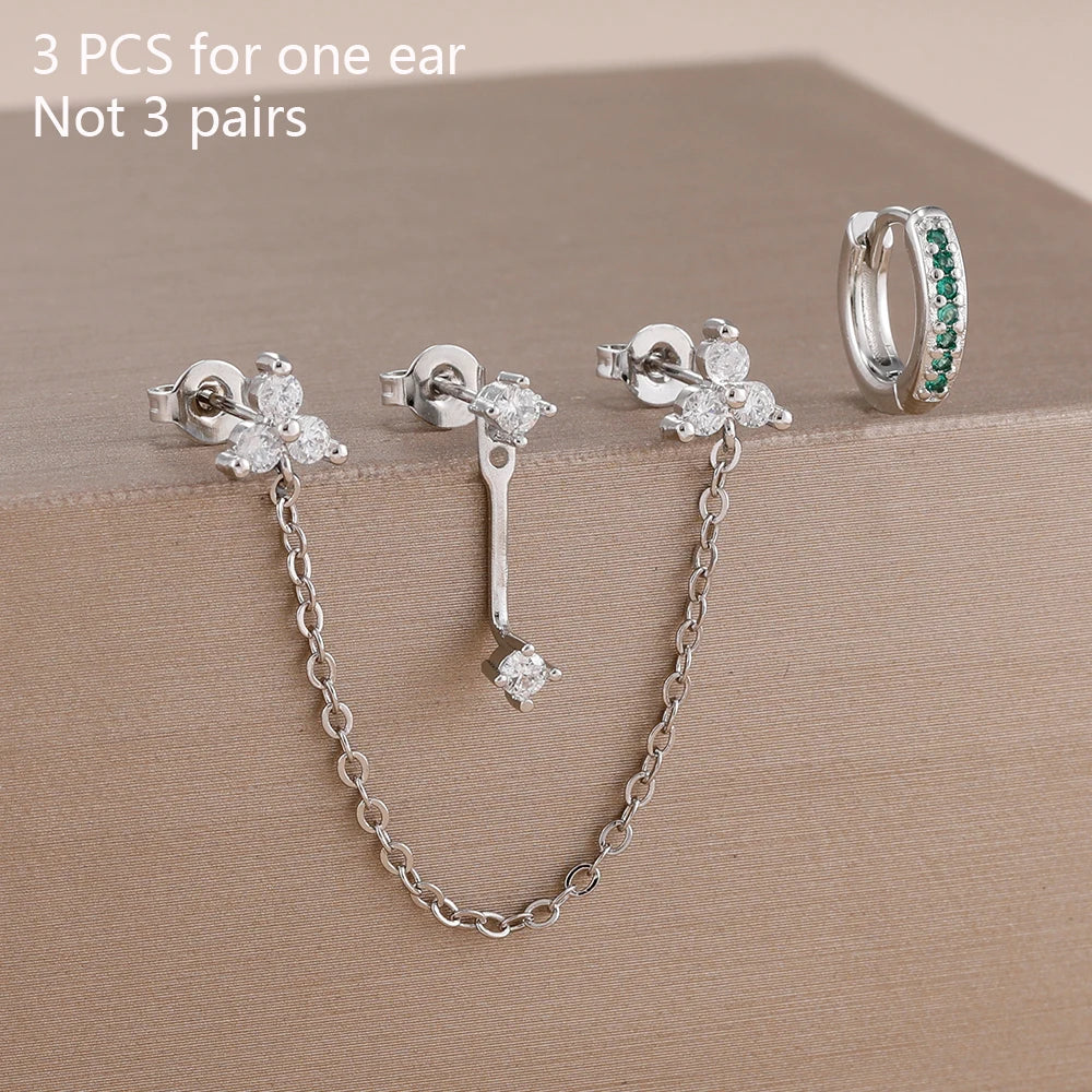 Boucles d'oreilles en chaîne à maillons doubles argentés avec des pierres de zircon vert sur fond neutre.