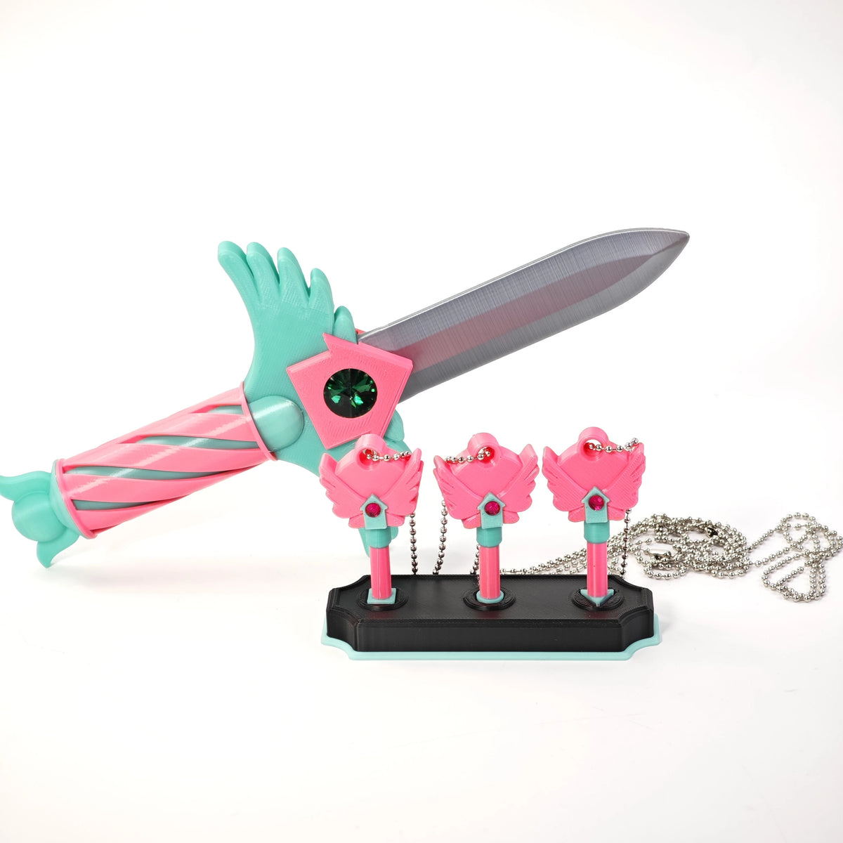 A set of four pink and teal dagger key necklaces with a silver blade and green handle displayed on a black base.