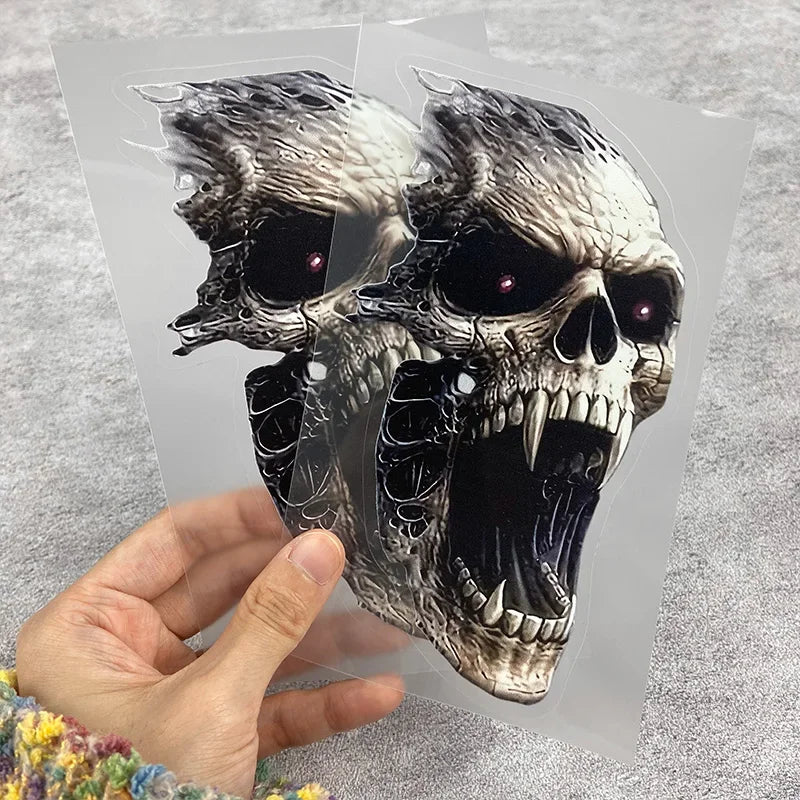A hand holds a clear vinyl skull decal featuring a detailed, menacing skull design for car windows or body.
