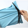 A hand is opening a light blue heavy-duty waterproof poly mailer bag, showing the black sealing strip.