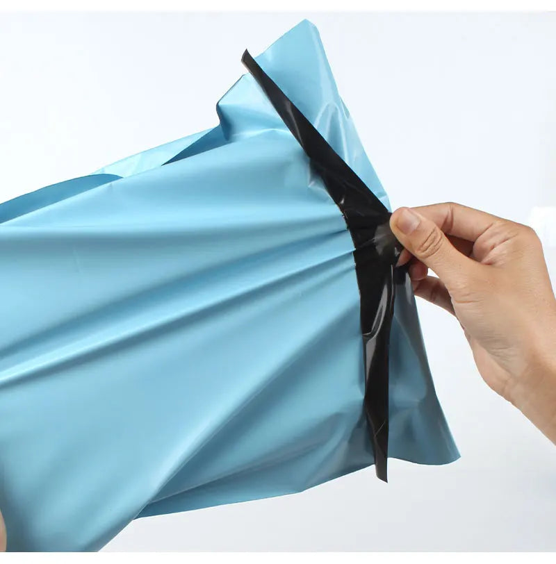 A hand is opening a light blue heavy-duty waterproof poly mailer bag, showing the black sealing strip.