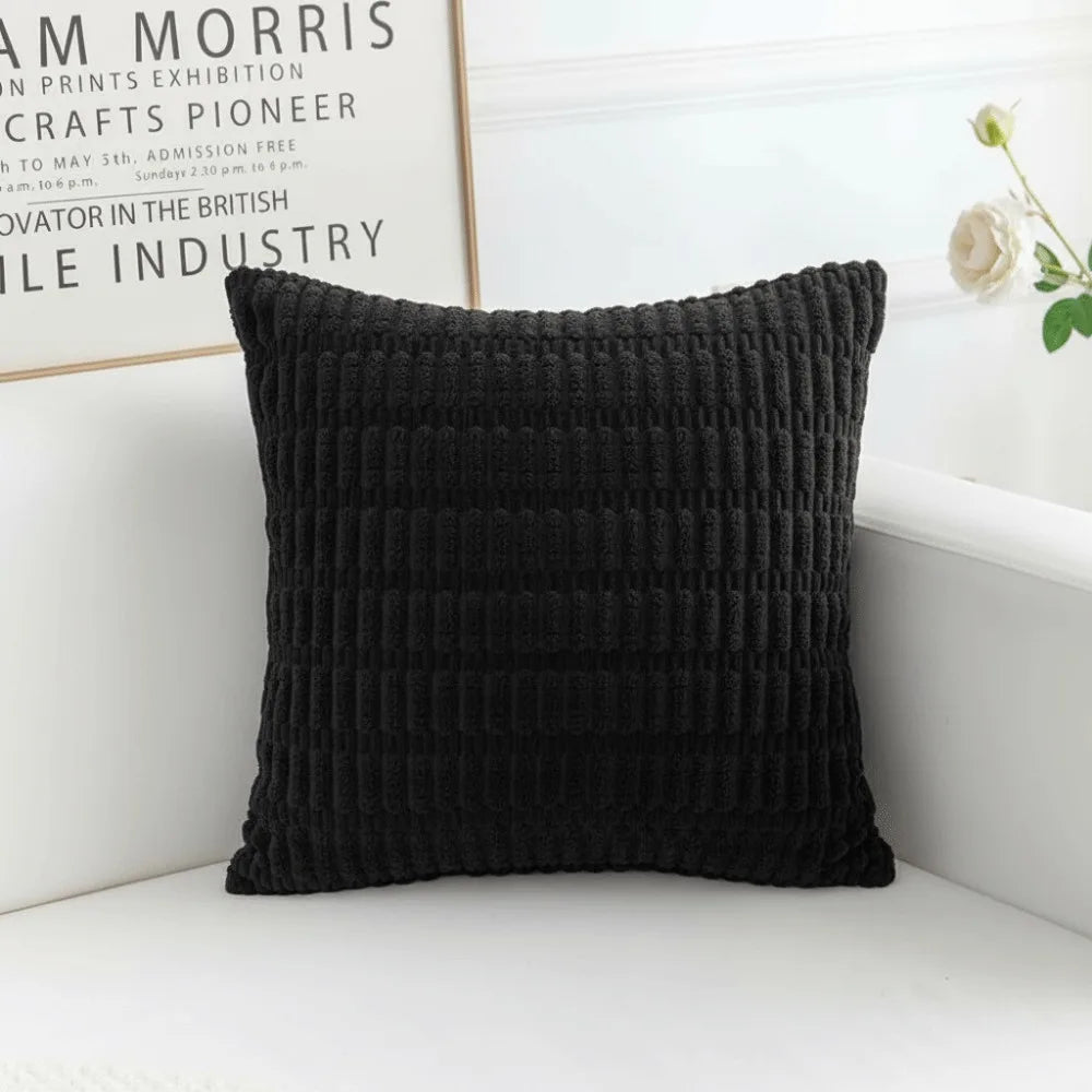 A black knitted pillowcase with a ribbed texture resting on a white surface.