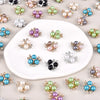 A collection of pearlized resin flower beads in various shades of green, purple, and blue scattered on a white surface.