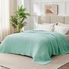 A light mint green soft muslin cotton blanket draped over a bed in a bright, modern bedroom.
