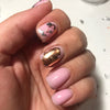 A hand displays a manicure featuring pink and gold metallic foil flakes on the nails.