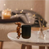 A dark brown dachshund coffee mug with a 3D puppy handle sits on a white table next to a glass holder.