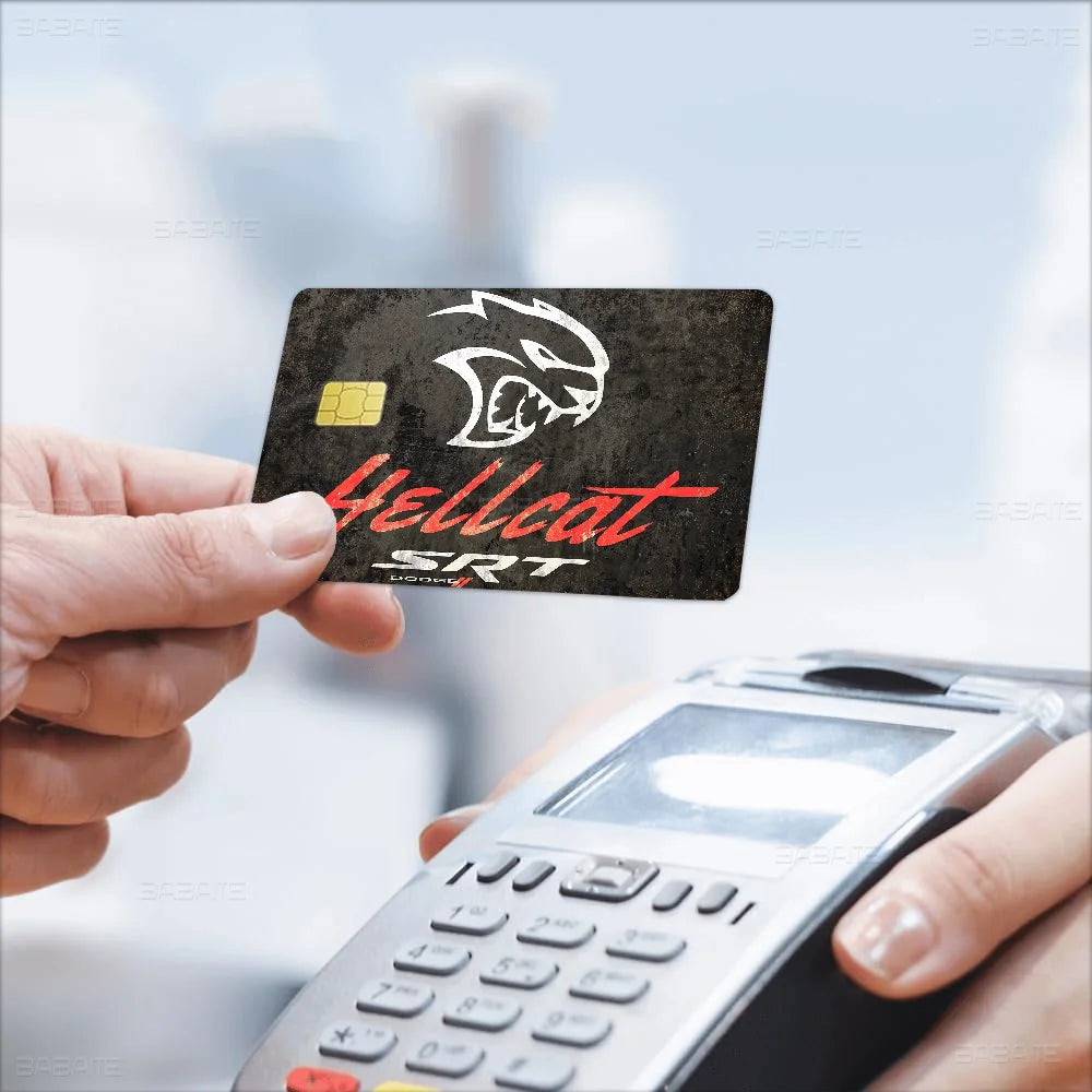A hand holds a credit card with a Hellcat SRT design printed on it, next to a handheld device.