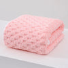 A pink plush coral velvet bath towel folded on a white surface.