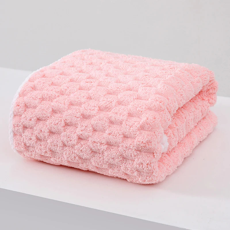 A pink plush coral velvet bath towel folded on a white surface.