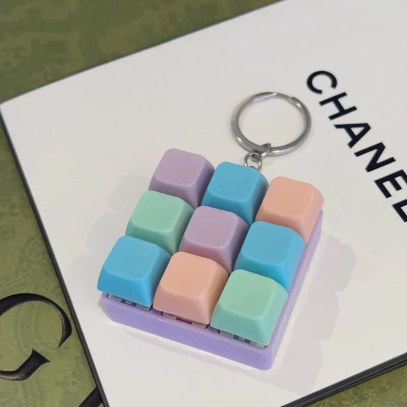 A purple tactile clicking keyboard keychain fidget toy with pastel colored buttons and a silver keyring.