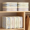 A display of stacked, light-colored fabric storage bags with handles on a wooden shelf.