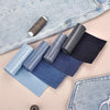 A collection of denim iron-on patches in various shades of blue and gray are displayed on a light pink background.