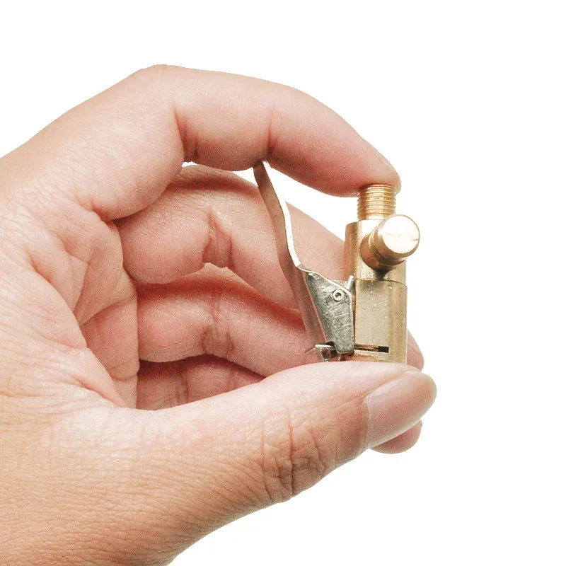 A hand holds a brass tire inflator chuck with a clip-on valve connector.