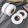 Rolls of white double-sided iron-on fabric adhesive tape lying on a gray cloth.