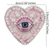 A heart-shaped patch featuring a purple eye surrounded by pink and white beads and rhinestones.