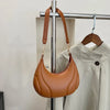 A brown leather crossbody bag with a padded flap and adjustable strap is displayed on a hanger.