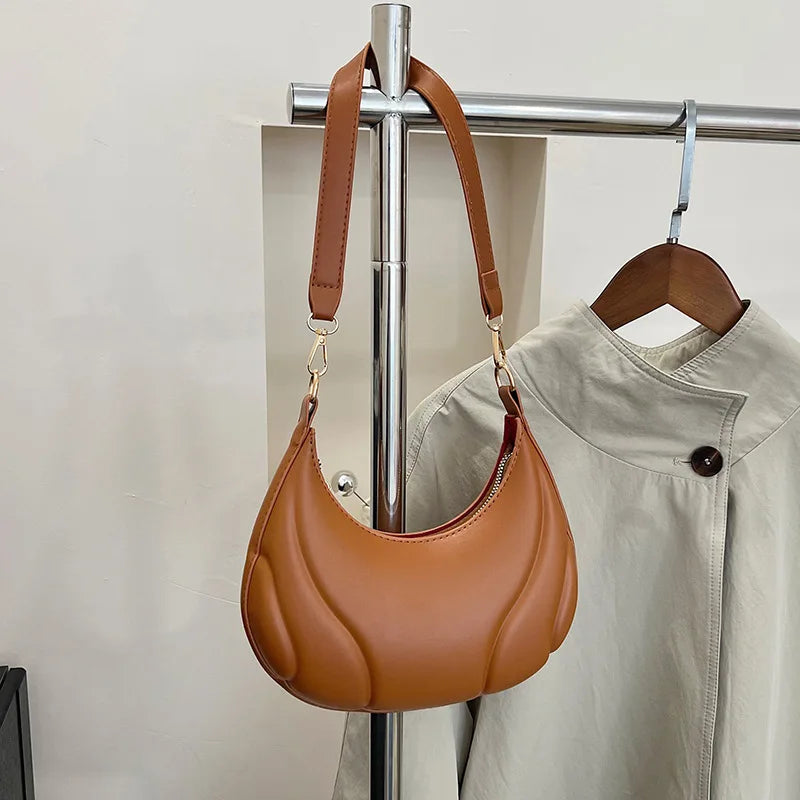 A brown leather crossbody bag with a padded flap and adjustable strap is displayed on a hanger.