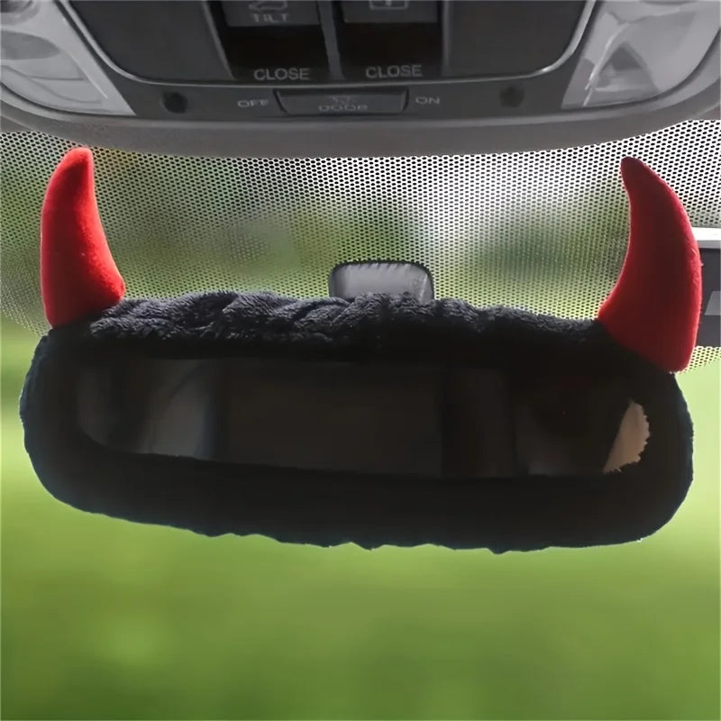 A black devil horn rearview mirror cover with red accents is shown against a blurred green background.