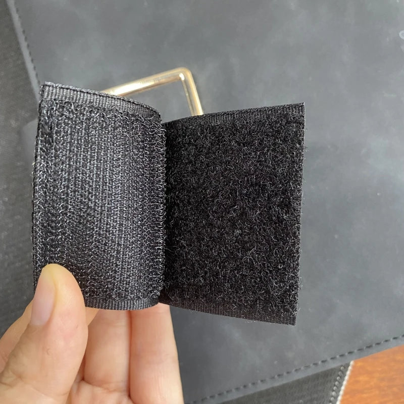A close-up of a black embroidered patch with a hook and loop backing being held by a hand.