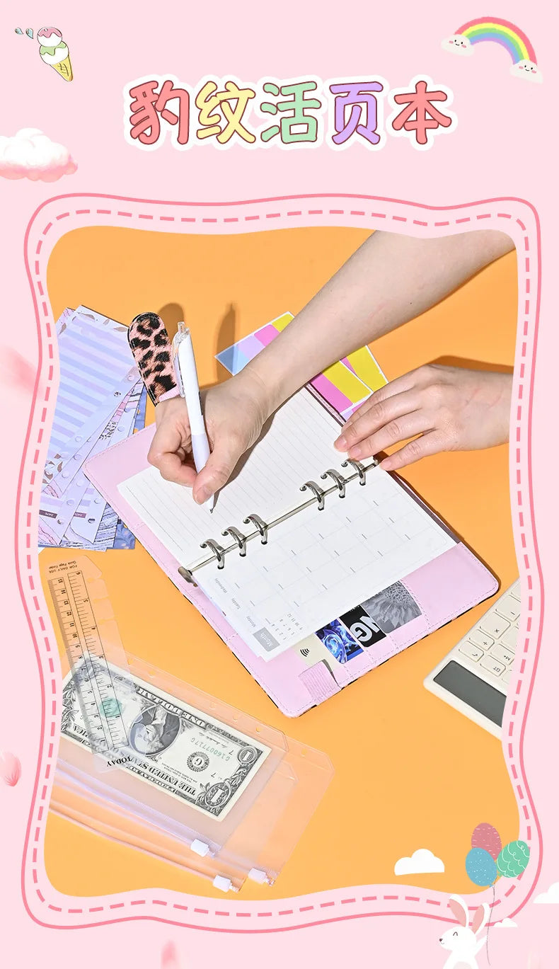 Eine Hand schreibt in einem rosa A6 Budgetplaner-Notizbuch neben Bargeld und einem Taschenrechner.