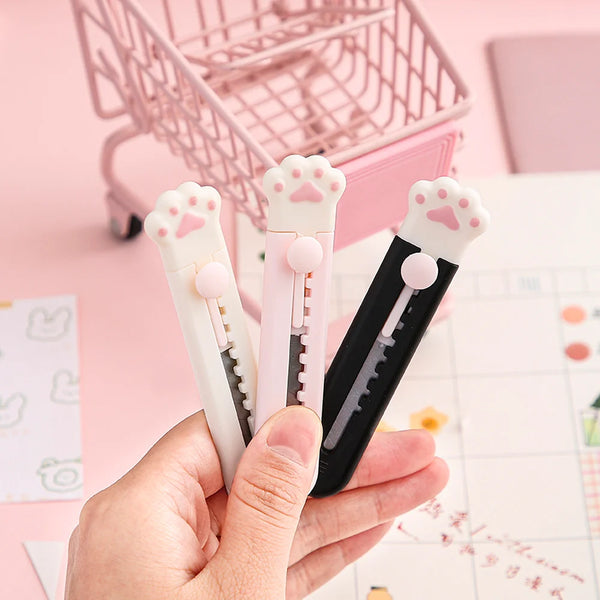 Une main tient trois mini outils ou ciseaux à griffes pour chats pour la création et la décoration sur une surface rose.